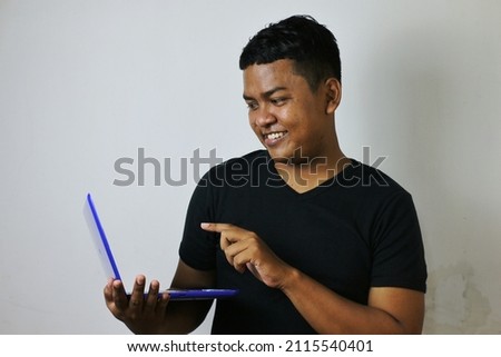 young asian man in black shirt holding laptop and pointing at screen with right hand and looking happy