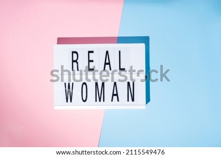 Real Woman text on the lightbox. Concept of feminism on a blue and pink background. Top view