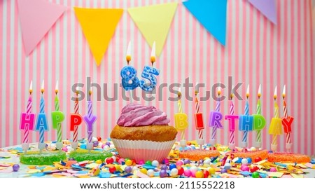 Happy birthday number 85. On a pink background, congratulations on the birthday of an eighty-five year old. Muffins with pink cream with a burning candle. Copy space.
