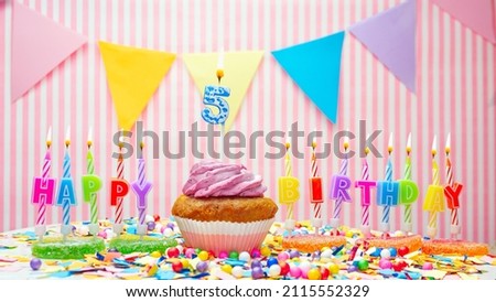 Happy birthday number 5. On a pink background, a happy birthday greeting for a five year old child. Muffins with pink cream with a burning candle. Copy space