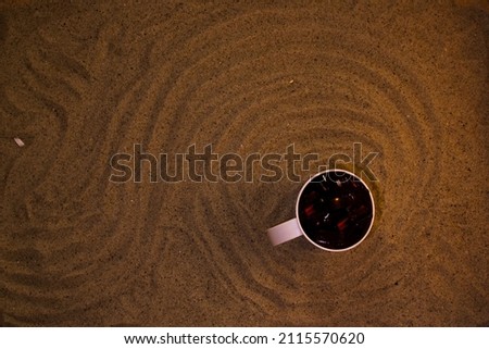 Cup filled with glass fragments on the sand with patterns 