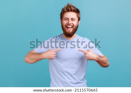 It's me! Portrait of ambitious bearded man with toothy smile, pointing fingers on himself, being confident and proud of his success and achievements. Indoor studio shot isolated on blue background. Royalty-Free Stock Photo #2115570665