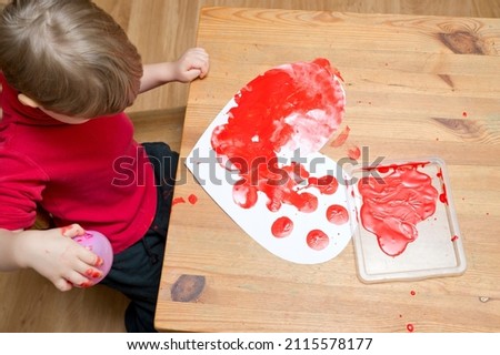 The child draws with red paint on heart shape paper. Valentine's Day theme. Fine motor skills, early education. Kids brain activities. Task idea for mothers to work with child’s at home.
