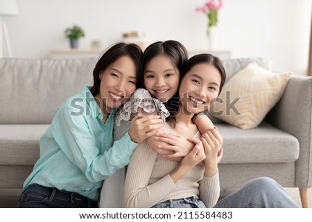 Warm relations concept. Young Asian woman with her cute daughter and mature mother hugging and smiling at camera indoors. Portrait of loving multi generation family embracing at home Royalty-Free Stock Photo #2115584483