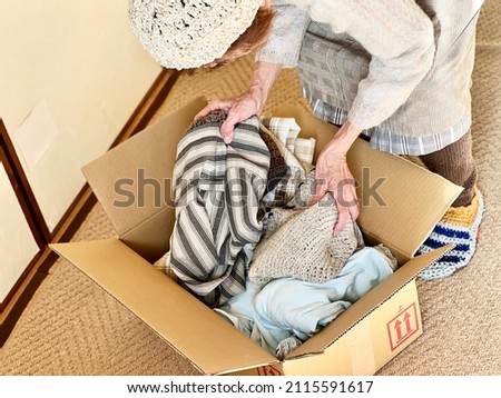 Hands of an elderly woman putting clothes in cardboard Royalty-Free Stock Photo #2115591617