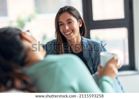 Shot of two smiling young women talking while drinking coffee sitting on couch in the living room at home. Royalty-Free Stock Photo #2115593258