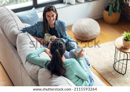 Shot of two smiling young women talking while drinking coffee sitting on couch in the living room at home. Royalty-Free Stock Photo #2115593264