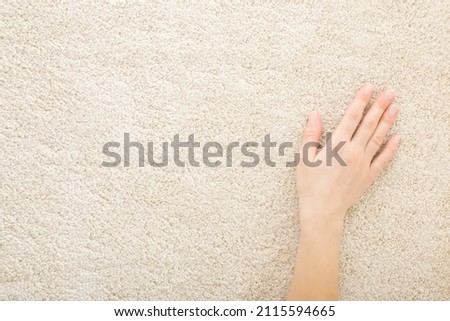 Young adult woman hand touching beige new fluffy home carpet. Closeup. Checking softness. Empty place for text.  Royalty-Free Stock Photo #2115594665
