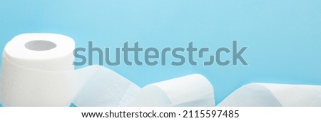 Soft, white unrolled toilet paper on light blue table background. Pastel color. Hygiene concept. Empty place for text or logo. Closeup. Wide banner.