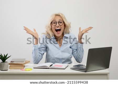 Portrait of overjoyed young businesswoman sitting at table with laptop against light background. Millennial female entrepreneur celebrating achievement or success at desk