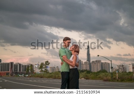Lovely mix young couple standing on the street in the metropolis on the sunset and cuddling. Love people and happiness. Skyscrapers on the background