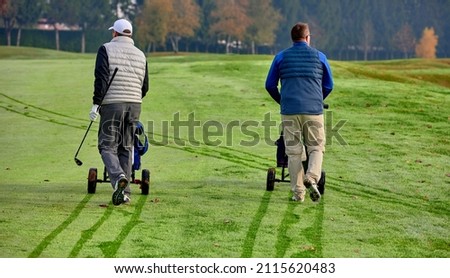 Golfers on a golf course in winter with frost covering the grass, pushing the cart up to the ball.