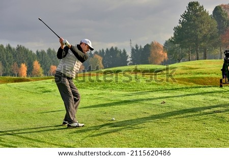 Golfer on a golf course in winter with wet grass, hitting the ball with a golf club. Royalty-Free Stock Photo #2115620486