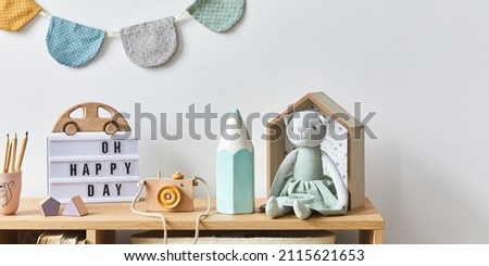 Stylish scandinavian newborn baby room with toys, plush animal, photo camera, dolls and child accessories. Cozy decoration and hanging cotton balls on the white wall. Copy space.