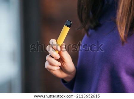 Yellow disposable electronic cigarette in a woman's hand. Modern smoking  Royalty-Free Stock Photo #2115632615