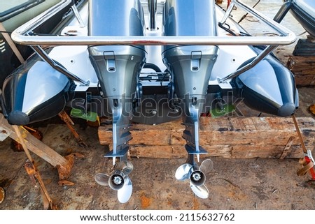 Two outboard motors at the stern of a motorboat resting on wooden blocks in dry dock. Royalty-Free Stock Photo #2115632762