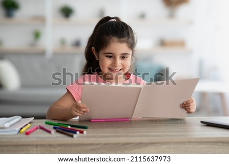 Education Concept. Portrait Of Cute Little Arab Girl Reading Book At Home, Excited Middle Eastern Female Child Study While Sitting At Desk At Home, Smiling Kid Doing Homework, Copy Space Royalty-Free Stock Photo #2115637973