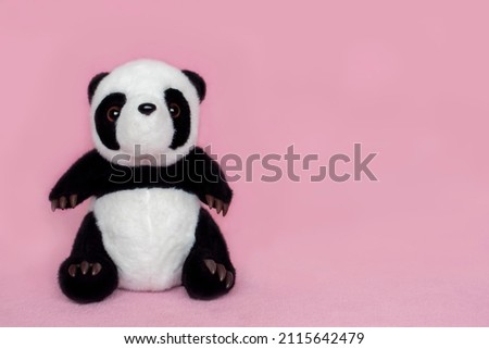 Soft toy panda for children on a pink background with empty space for text