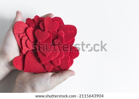 Hands holding a large pile of bright red hearts light background copy space.
