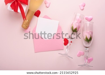 Valentines day greeting card with champagne bottle, gift box, red ribbon and envelope with blank note mockup inside on pink background. Top view with space for greetings. Greeting card with copy space
