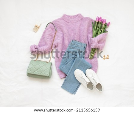 Lilac knitted sweater, blue jeans, white sneakers, green bag, bouquet of tulips flower lie on white background. Overhead view of woman's casual outfit. Trendy stylish women clothes. Flat lay, top view Royalty-Free Stock Photo #2115656159