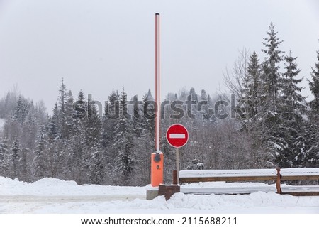 Automatic barrier and entrance to the parking lot in the snowy winter forest. Automobile and road infrastructure, road signs and pointers.