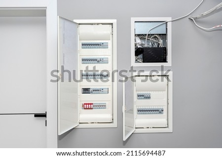 Two open electrical boxes with fuses and one multimedia box, placed in the garage in the gray wall. Royalty-Free Stock Photo #2115694487