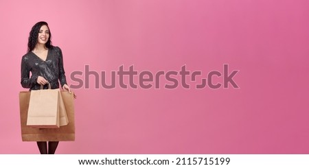 A young woman holds a large brown paper bag and looks down in surprise. Banner. Young woman on a pink background holding shopping bags on a pink background. Place for a logo.