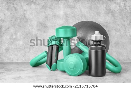 Fitness equipment on a gray concrete background with copy space. Dumbbells, sport bottle of water, jump rope, leg trainer, gymnastic ball, front view. Home workout. Fitness and activity.