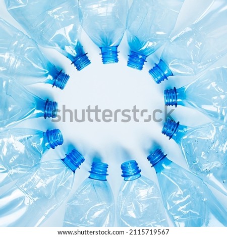 Crumpled blue plastic PET bottles lie in a circle with their necks in the center on a white background, in the middle there is an empty space. Square image format. Royalty-Free Stock Photo #2115719567
