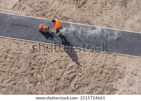 New road construction worker laying asphalt surface on walkway work. Sidewalk construction asphalt work road tarmac. Hot asphalt paving road construction site work man vibratory plate compactor rammer Royalty-Free Stock Photo #2115724661