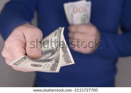 A man in a blue jumper holds money in his hands, a stack of 100 dollars blurred and close-up of money 100 dollars 200 dollars.Money concept Royalty-Free Stock Photo #2115727700