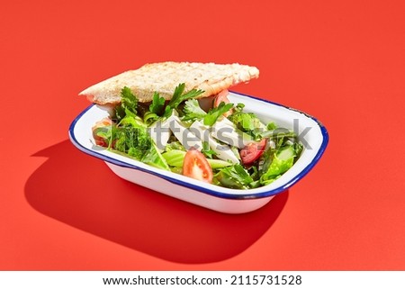 Vegetarian green salad on trendy red background with hard shadow. Green bowl with vegetables and tofu in minimal style. Contemporary food menu. Healthy food in modern concept
