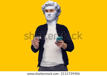 Abstract modern collage. The man with the plaster head of David Cheerful sports red-haired guy conducts online payment with smartphone on a yellow background. Royalty-Free Stock Photo #2115739406