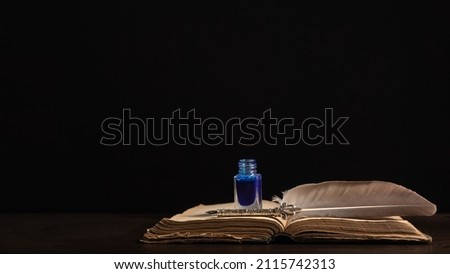 Quill pen and inkwell resting on an old book concept for literature, writing, author and history Royalty-Free Stock Photo #2115742313