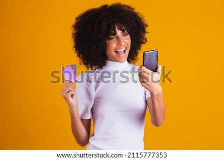 Photo of beautiful excited dark-skinned lady holding plastic credit card showing new phone model advising online payment yellow color background