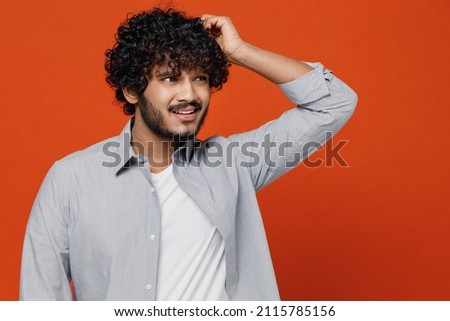 Confused preoccupied sad embarrassed upset young bearded Indian man 20s years old wears blue shirt looking aside think put hand on head have no idea isolated on plain orange background studio portrait Royalty-Free Stock Photo #2115785156