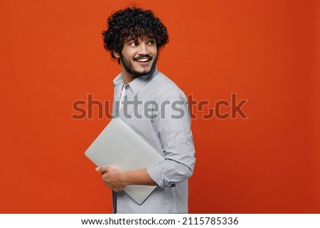 Fascinating fun young bearded Indian man 20s years old wears blue shirt hold use work on laptop pc computer looking behind keeping mouth wide open isolated on plain orange background studio portrait Royalty-Free Stock Photo #2115785336