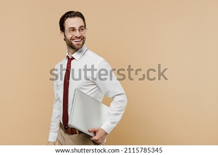 Young happy successful employee business man corporate lawyer 20s in white shirt red tie glasses work in office hold use laptop pc computer look aside on workspace isolated on plain beige background Royalty-Free Stock Photo #2115785345