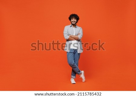 Full size body length confident happy young bearded Indian man 20s years old wears blue shirt hold hands crossed isolated on plain orange background studio portrait. People emotions lifestyle concept Royalty-Free Stock Photo #2115785432