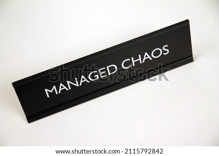 Managed Chaos, metal black and silver sign on a white shelf in office life