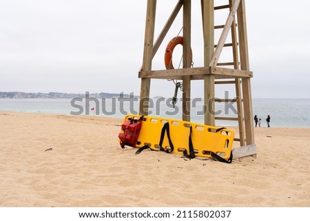 Yellow medical backboard leaning on wooden lifeguard tower on cloudy day in Algarrobo beach, Chile Royalty-Free Stock Photo #2115802037