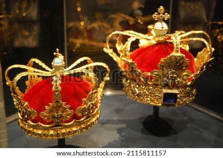 A pair of gold royal crowns with red velvet and bejeweled with multicolored jewels. Royalty-Free Stock Photo #2115811157