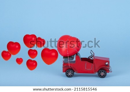 Red retro car carrying hearts for Valentine's day on bright blue background. Creative concept of love. Copy space