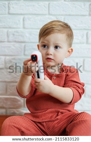 Smiling child holding an electric body temperature meter in his hands