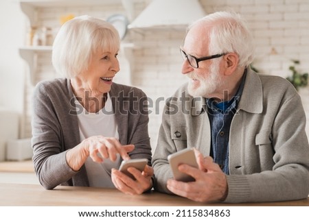 Smiling caucasian senior elderly couple grandparents spouses using smart phones cellphones together, surfing social media, e-banking, e-commerce at home kitchen, online shopping on application Royalty-Free Stock Photo #2115834863