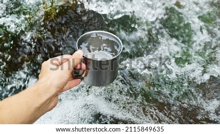 Hand holding cup with pure waterfall drinking water. 