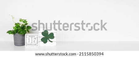 St Patricks Day decor on a white shelf. Shamrock plant, shabby chic wood calendar and sign against a white wall banner. Copy space.