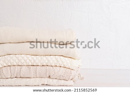 Pile of cozy white knitted clothes for cold weather. Comfort organic sweaters. Hygge style idea