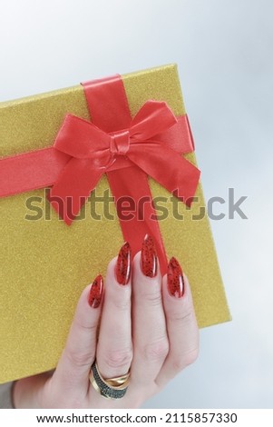 Female hands with long nails and red manicure hold a box with a gift for the holiday.